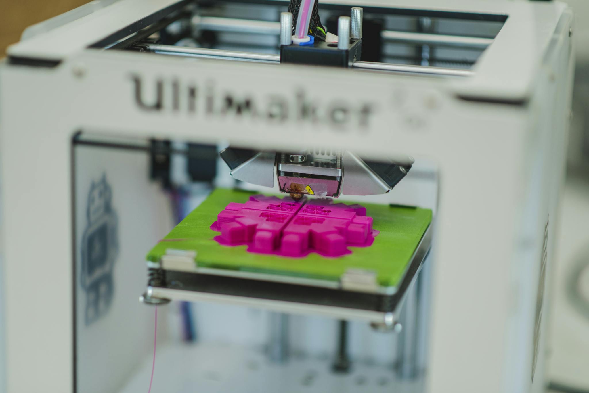 An Ultimaker 3D printer prints a neon pink shape on a green platform