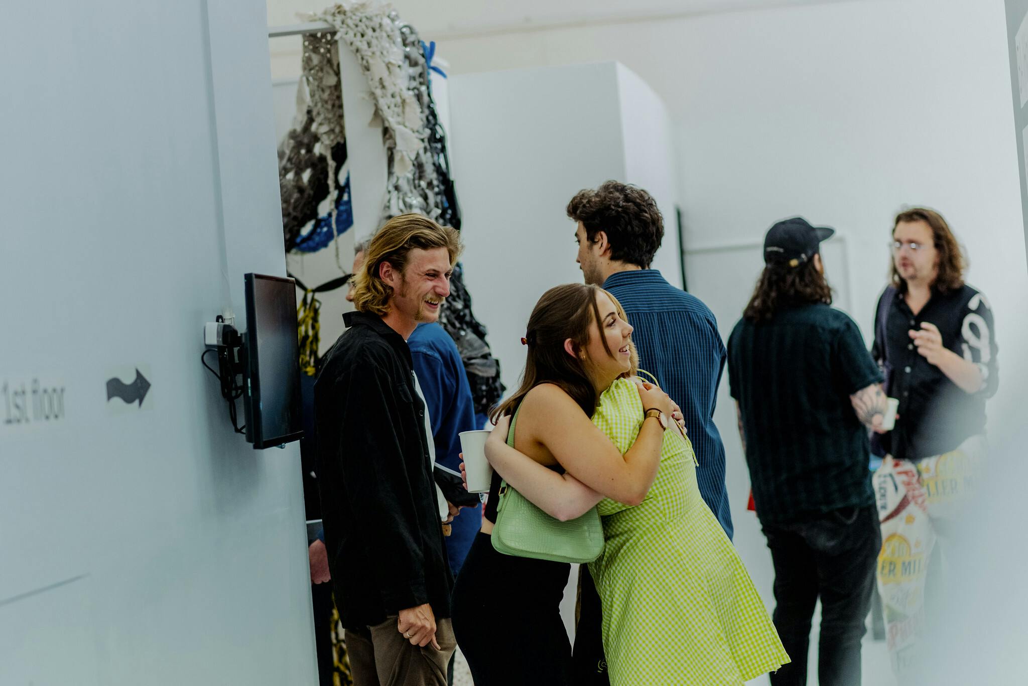 A girl in a green dress embraces a friend at an art exhibition