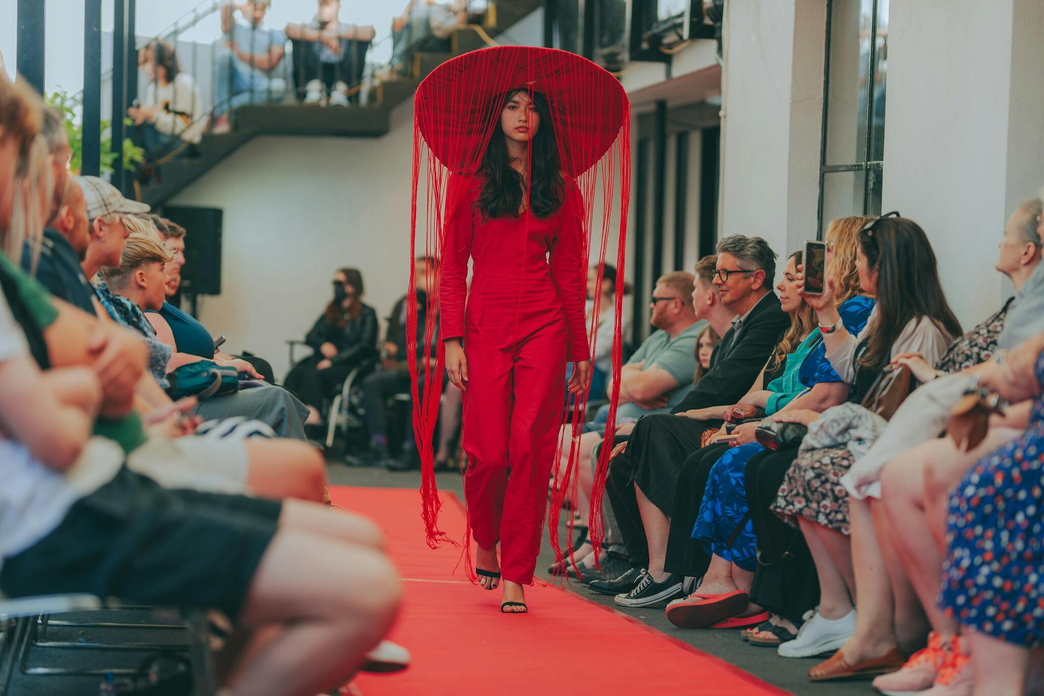 A model wearing a red outfit walks down the catwalk at our Pre Degree Summer Show in June 2023