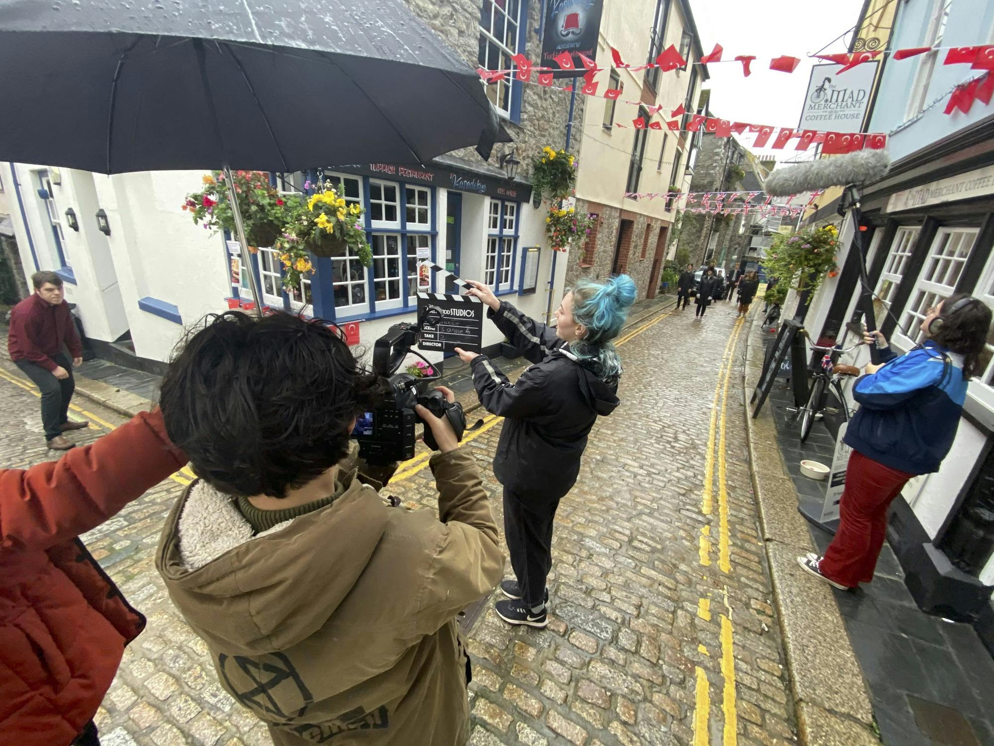 On a cobble stoned street in Plymouth, two students look through the lens of a professional camera aimed at a girl with a black film clapper ready to shoot the scene.