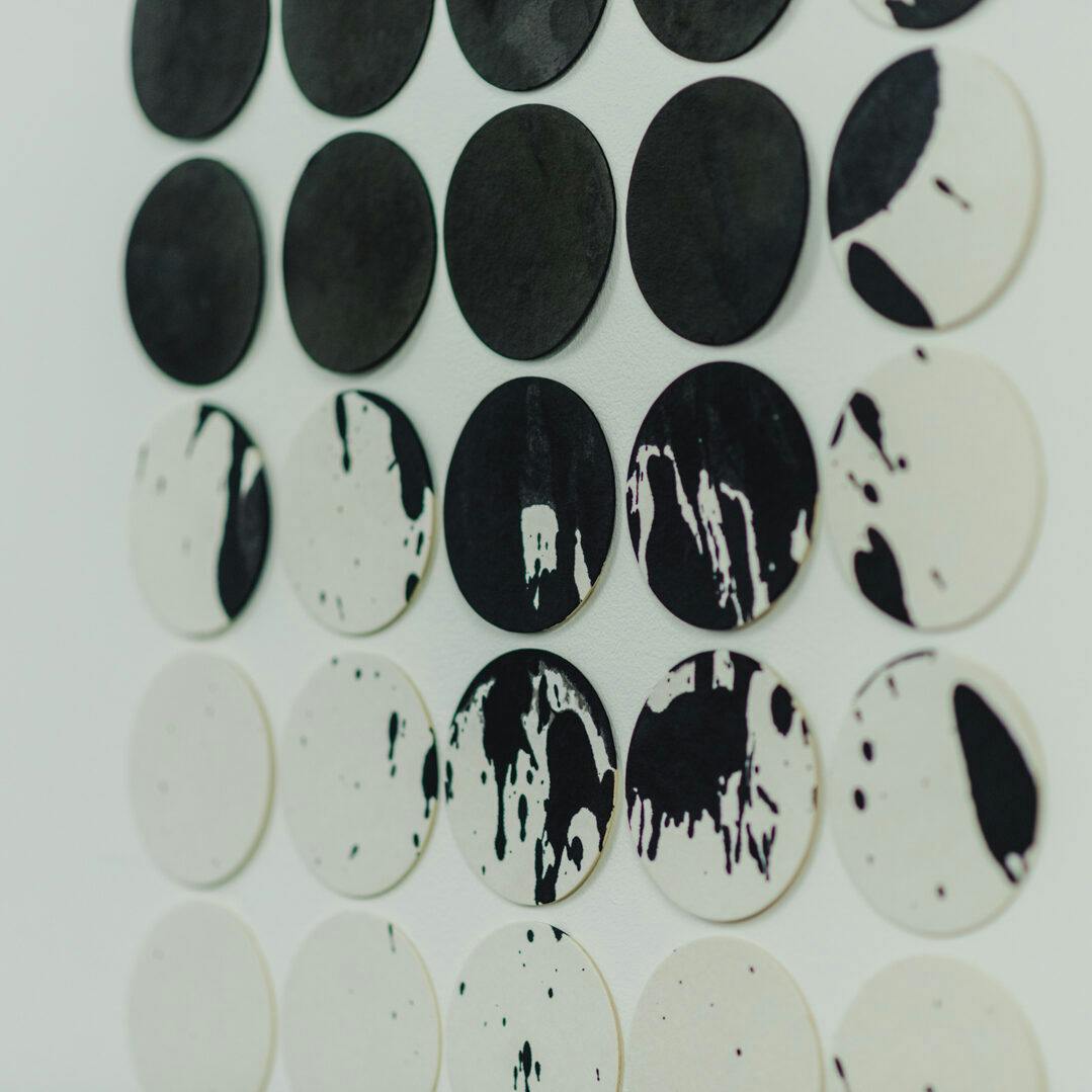 Black and white circular pieces mounted on a wall some splattered with black on show at the Extended BA Summer Show in 2022