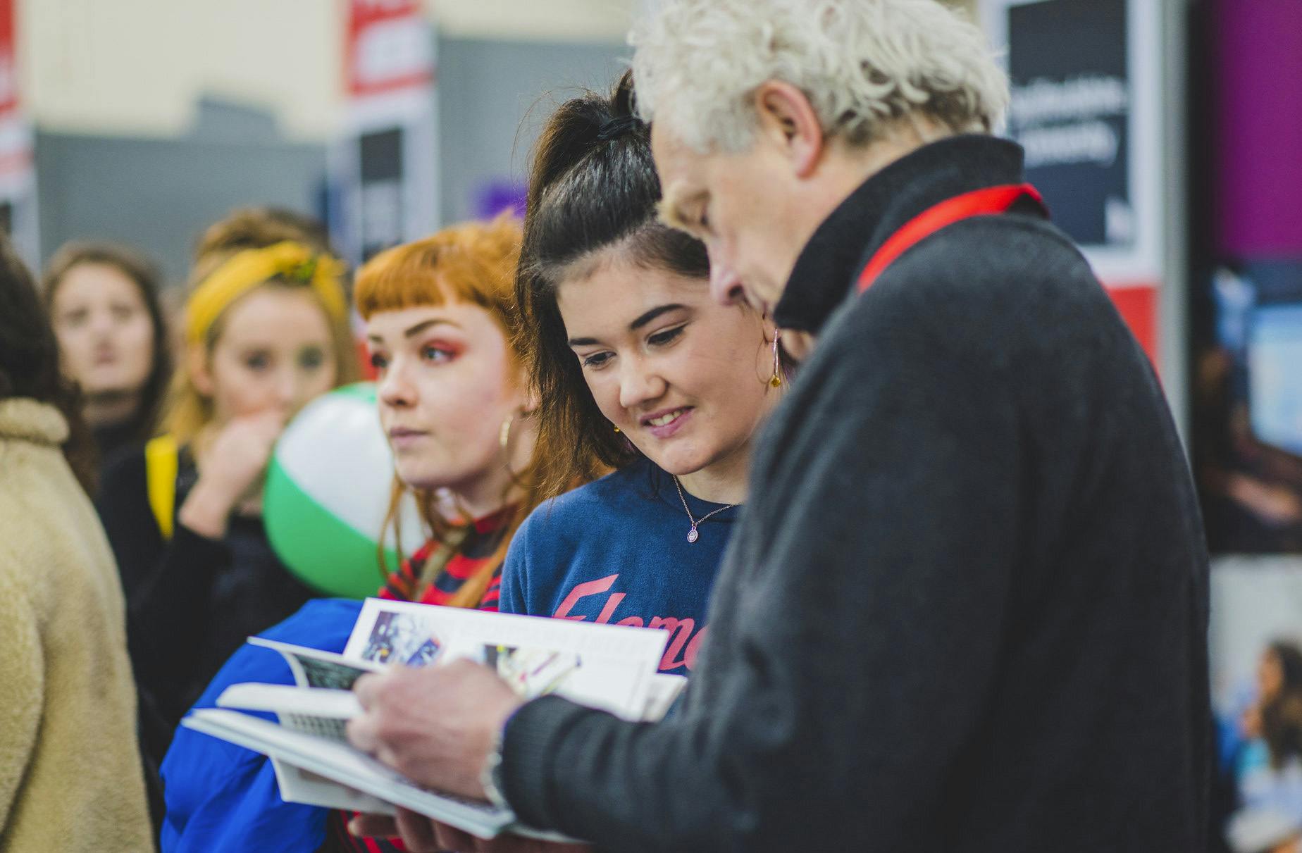 A member of the Plymouth College of Art team speaks to a student showing them a prospectus at a university fair event