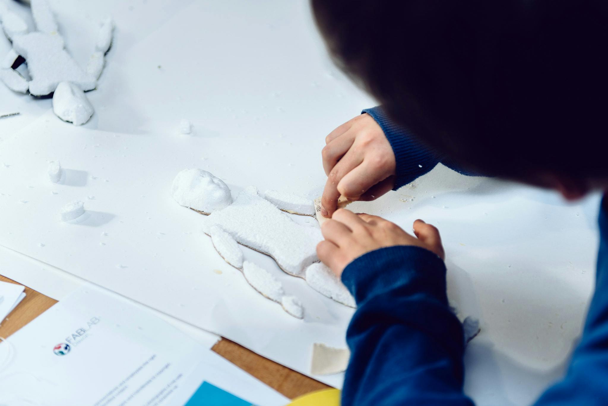 A young boys hands are shown making a 3D printed puppet on a table.