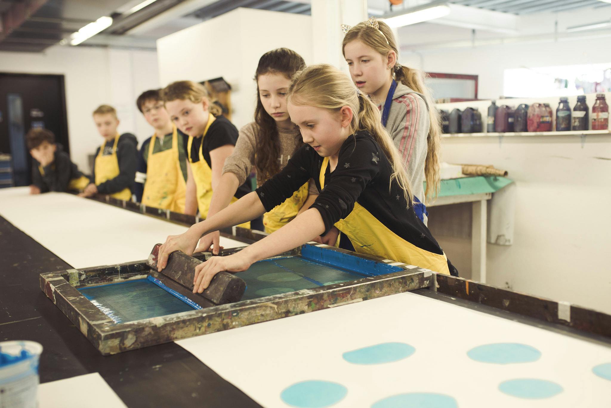 Group of young people in aprons having a go at screenprinting in Plymouth College of Art's textile workshop
