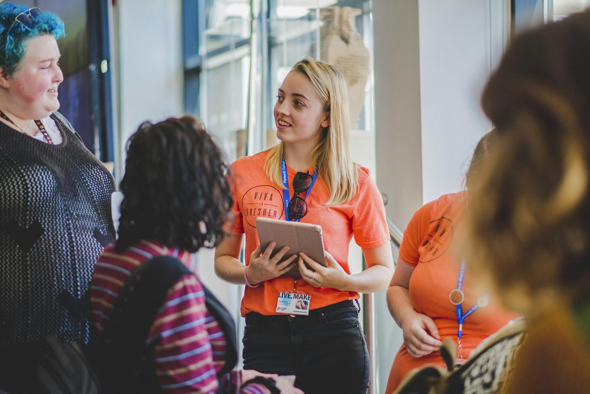 A blond haired student wears and bright orange Students' Union tshirt and talks to a group of four people at the annual Freshers Event