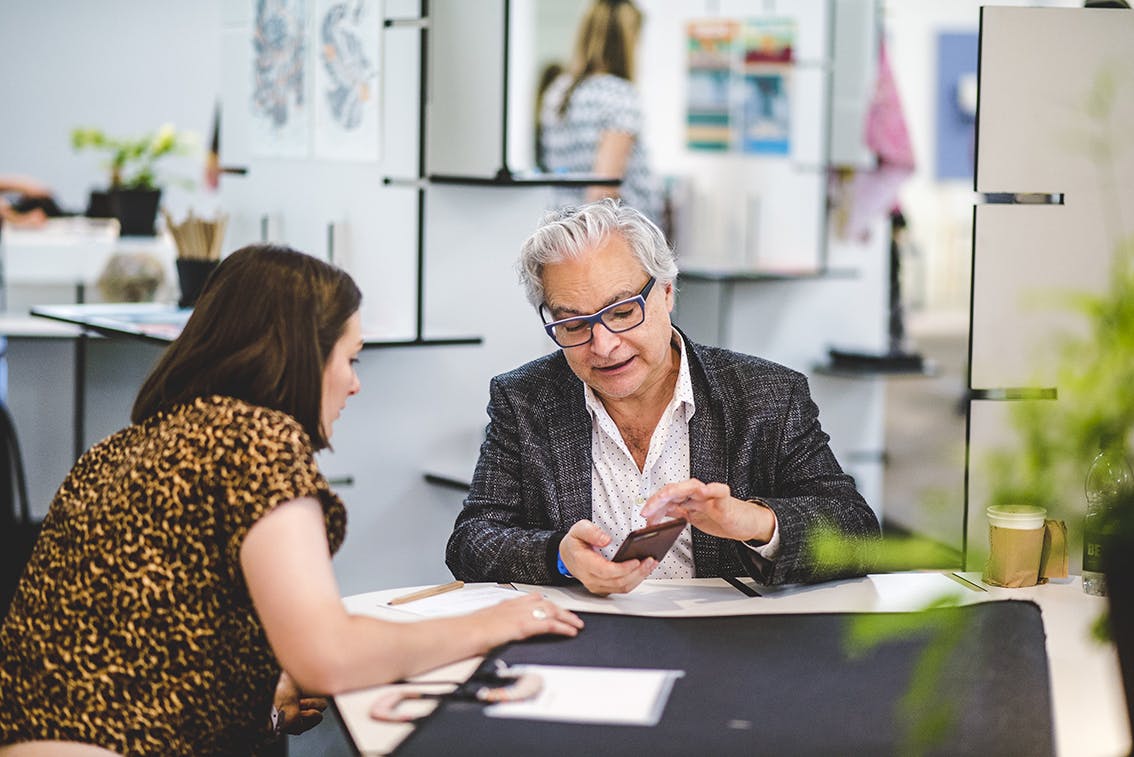 London Design Fair 2017 A woman shows her portfolio to an older man with glasses sitting at a desk at London Design Fair