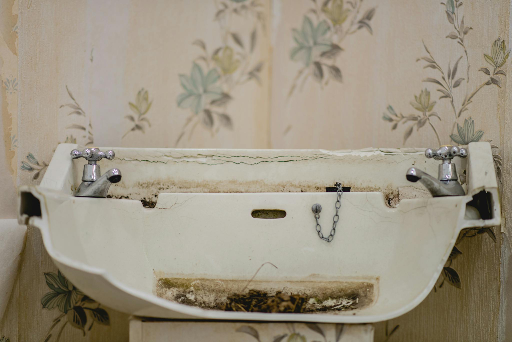 Image shows a broken ceramic sink which is dirty and rusted
