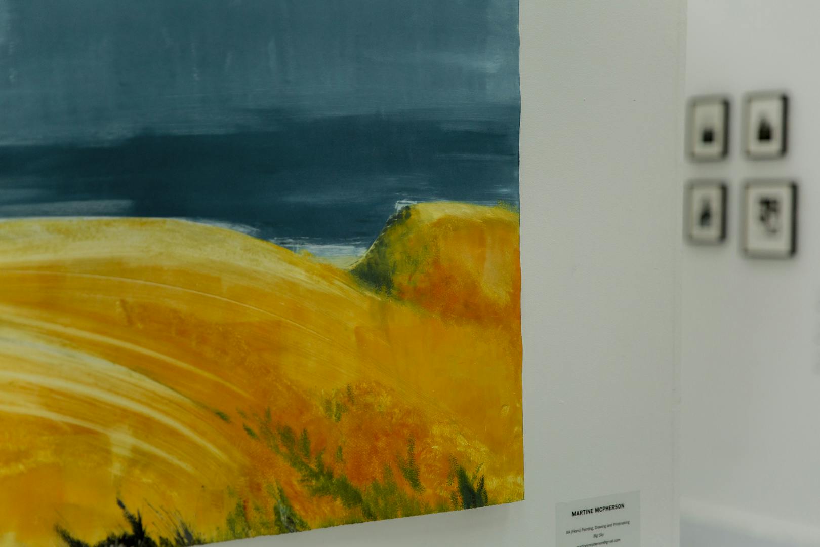 A close up shot of Martine's work in exhibition, with the painting featuring a landscape image and blue and orange colour tones
