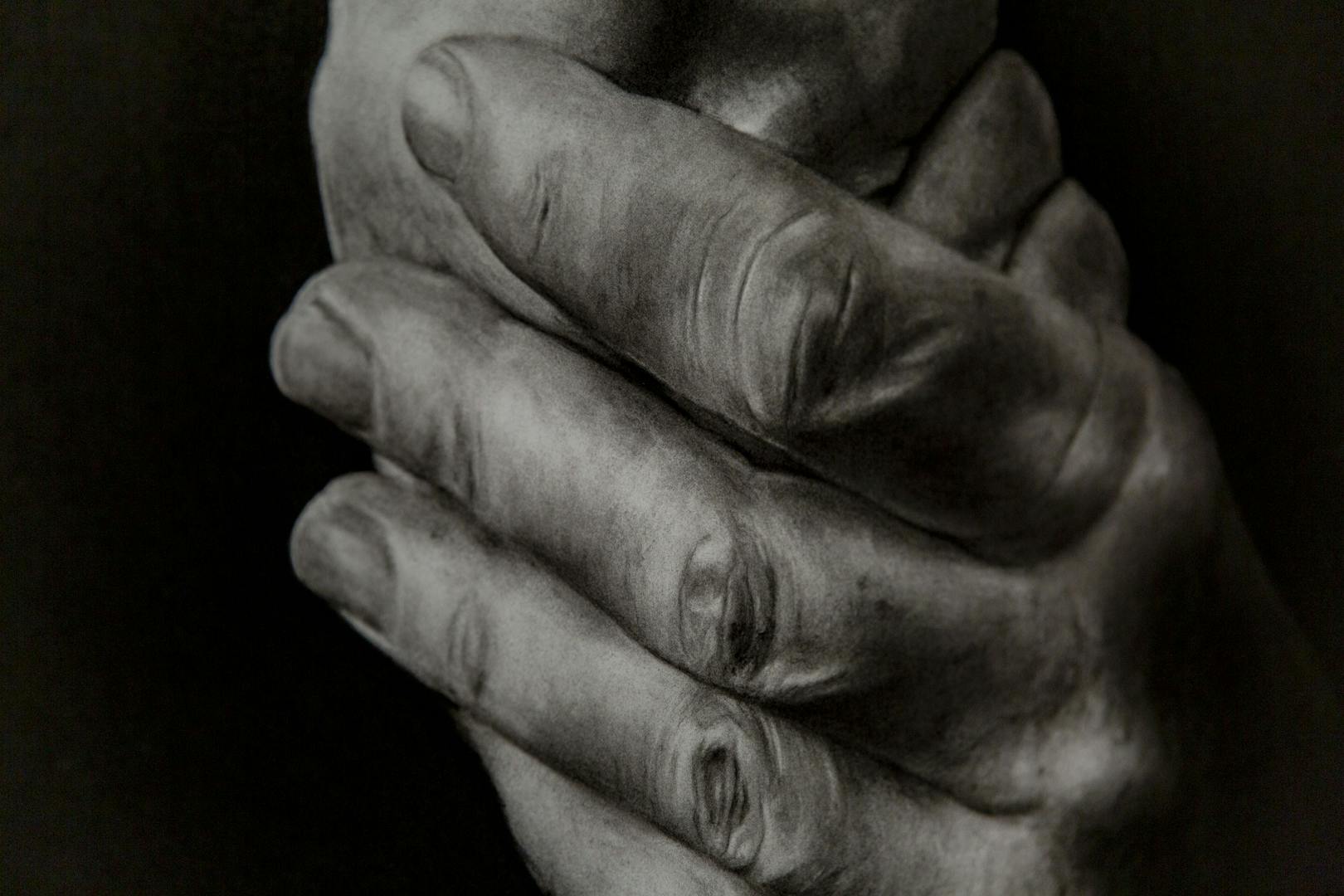 Image shows a black and white or grey scale hand drawn image of two hands clasped together