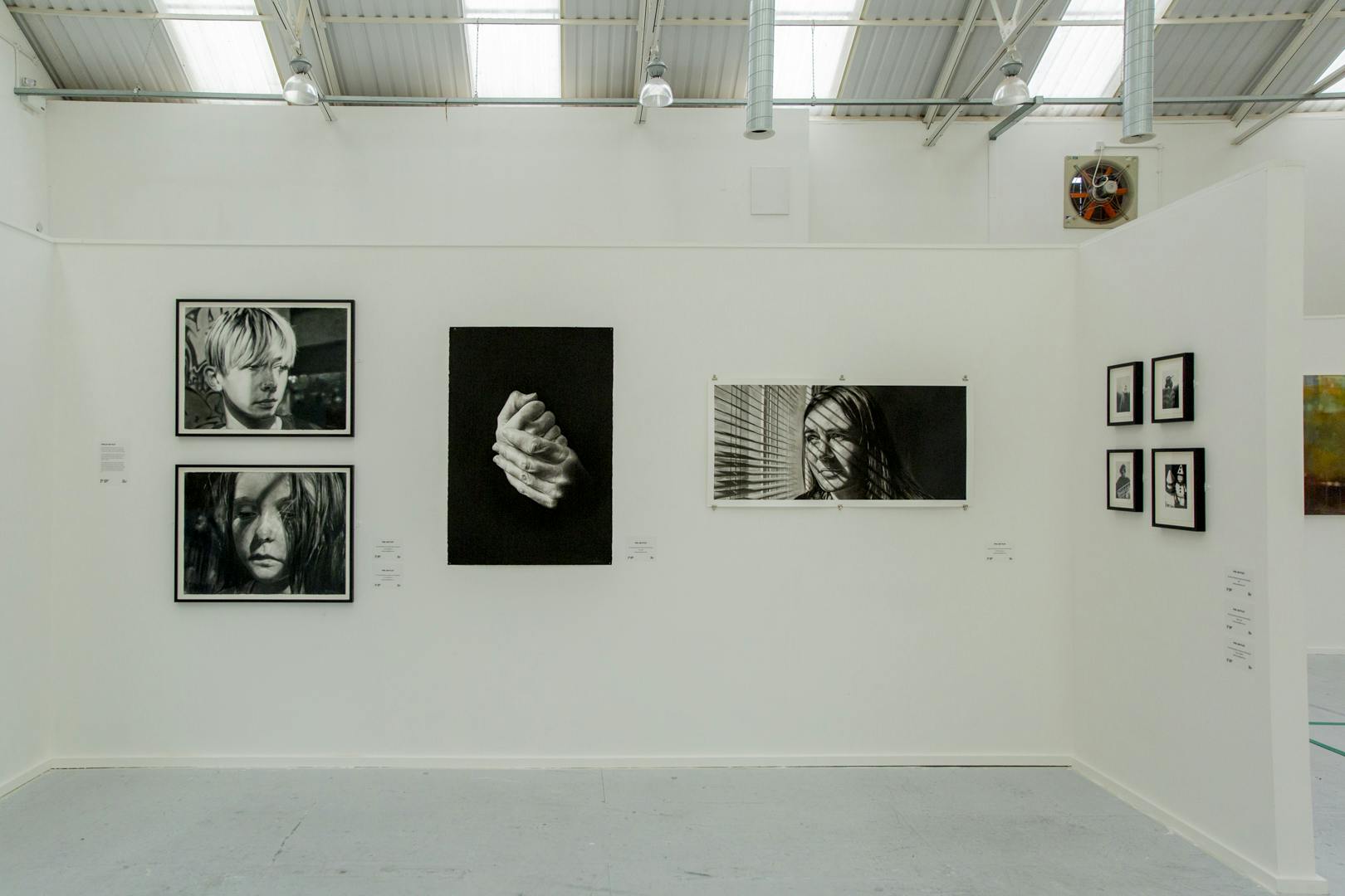 Image shows Phillip's hand drawn grey scale work in an exhibition setting featuring the drawings in black frames on a neutral white background
