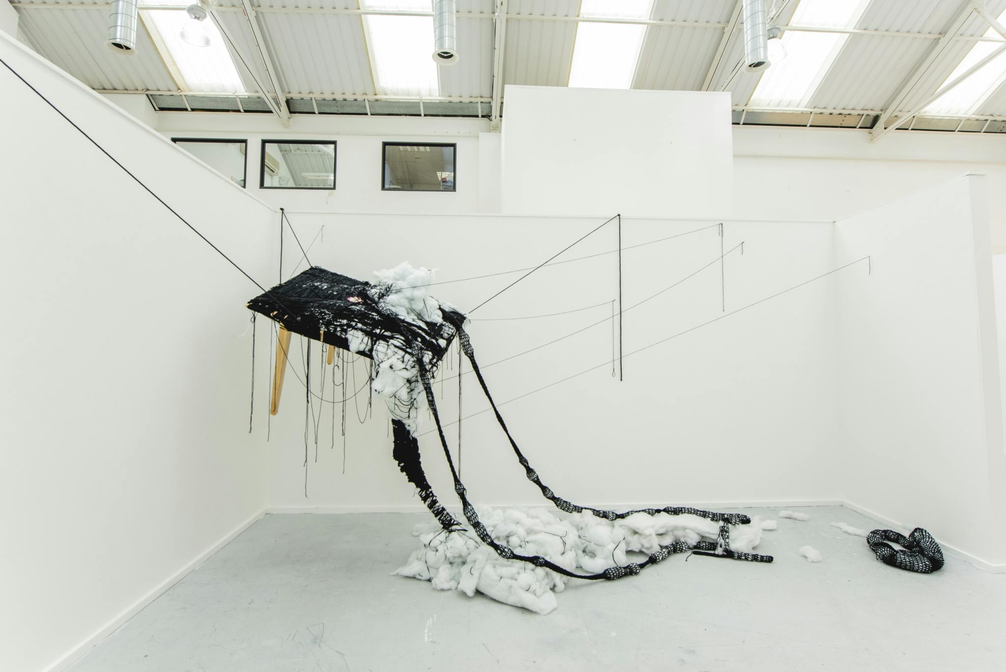 Image shows an art installation made up of a table, black wool, stuffing and thread
