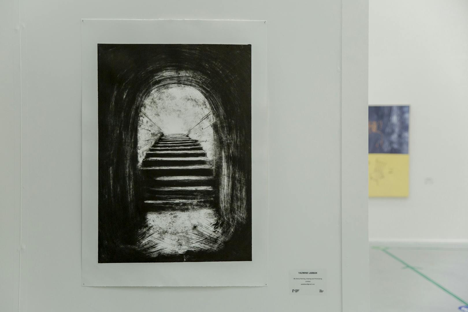 Image shows Yazmine's image of a black and white/grey scale tunnel or archway with some stairs behind it. In the background you can see another student's work in exhibition.