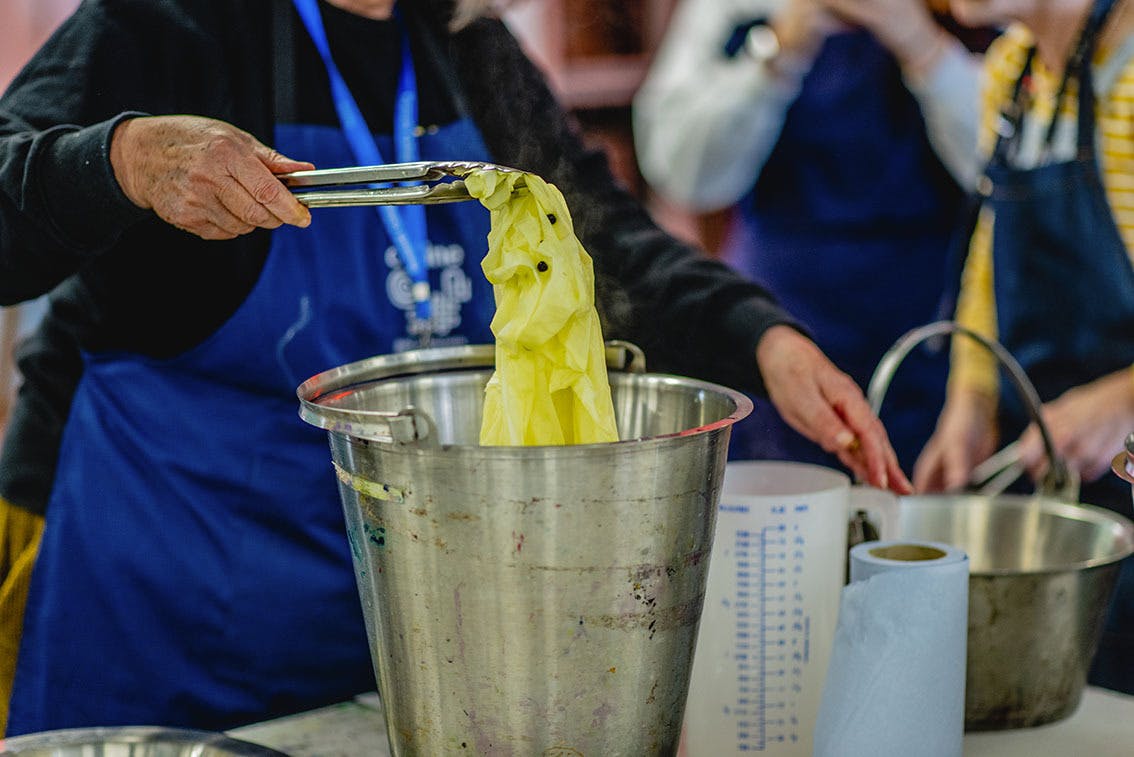 Textiles Natural Dyeing Workshop with Jane Deane in November 2021 removing yellow fabric from bucket of dye with tongs