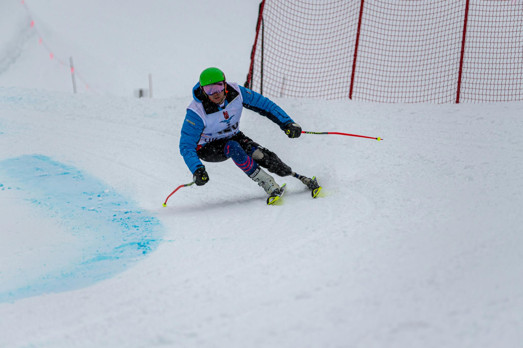 A skier from the Armed Forces Para-Snowsport team crouches low as they turn around a bend on a snowy slope