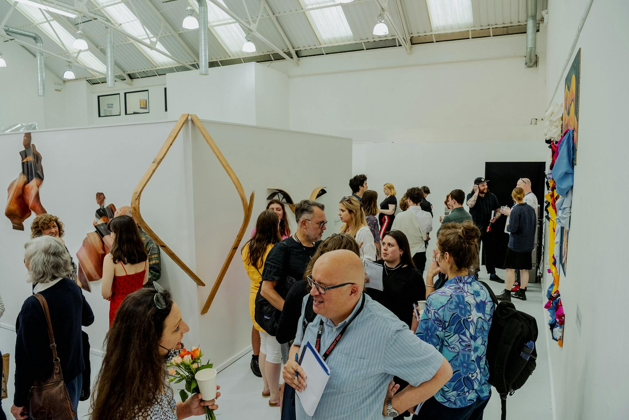 A large white exhibition space is busy with people viewing fine art sculptures