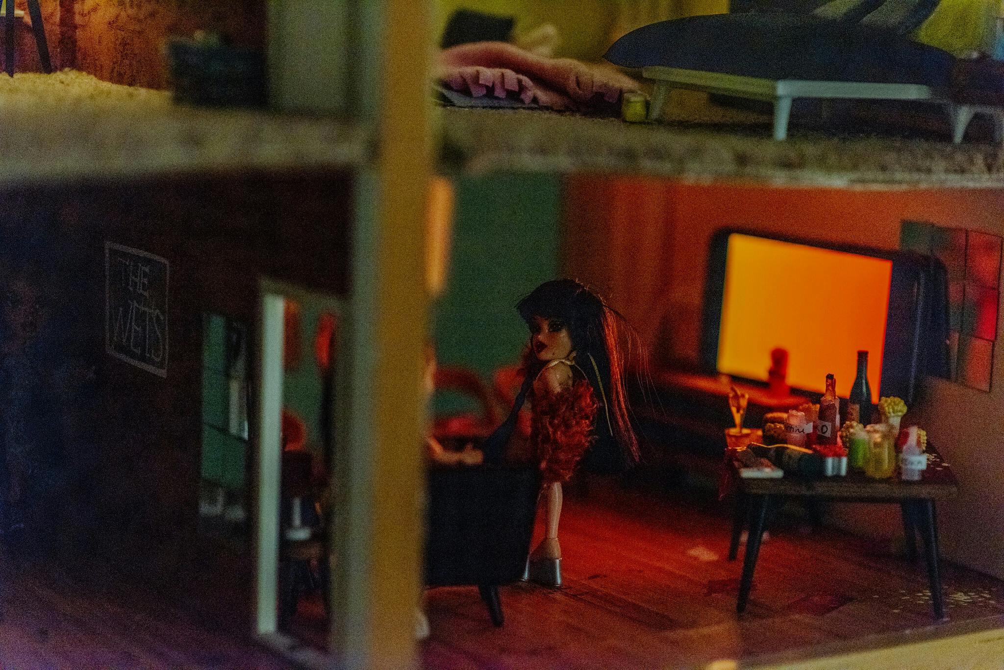 A close up view of a dolls house with dolls at a party with red light from a small tv screen