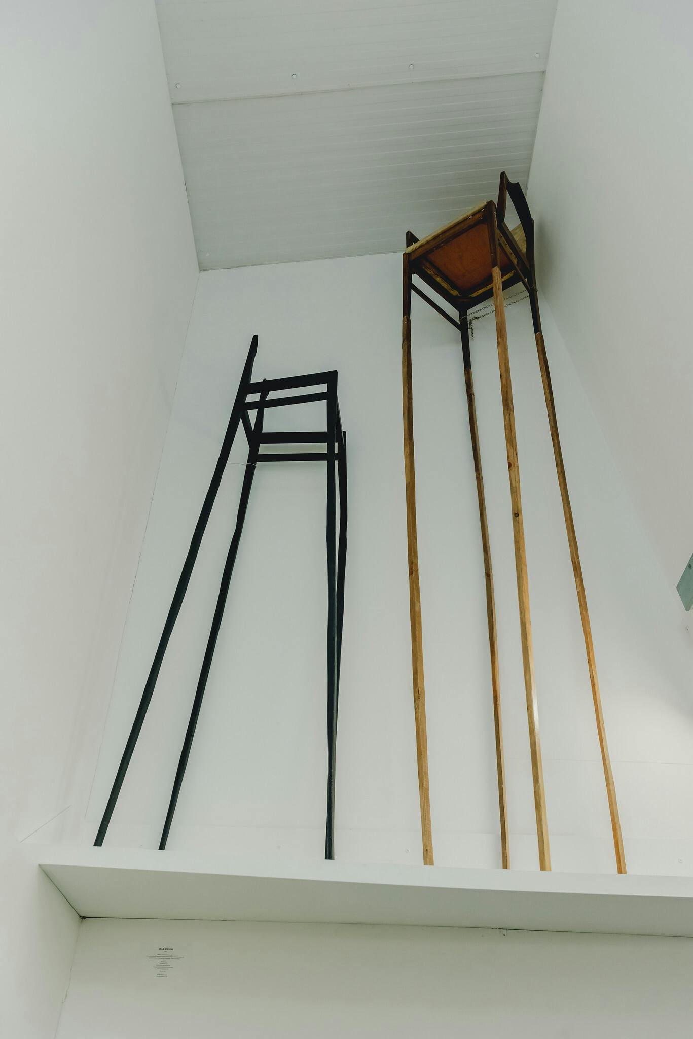Max Wilsons sculptures show a black chair and a wooden chair with tall five to six foot legs