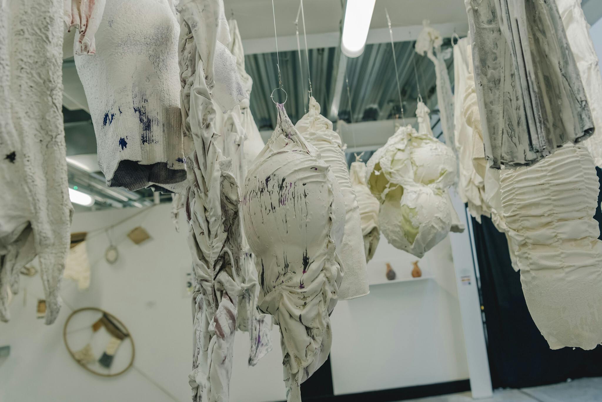 White misshapen sculptures hang from the ceiling in a white studio