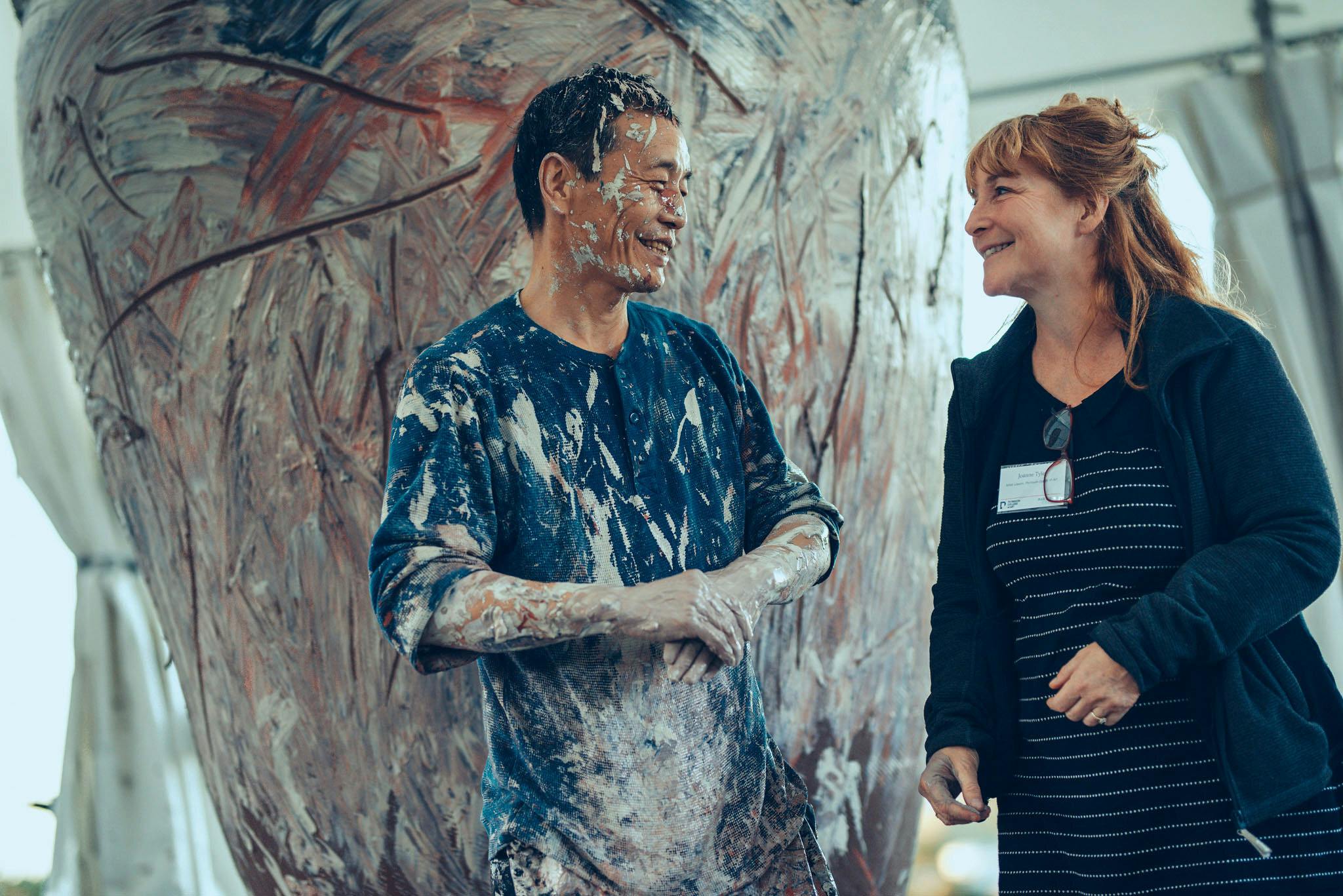 Ceramicist Kang-hyo Lee smiles with Jo Tyler at the culmination of his performance. His clothes and hands are covered in ceramic slip.