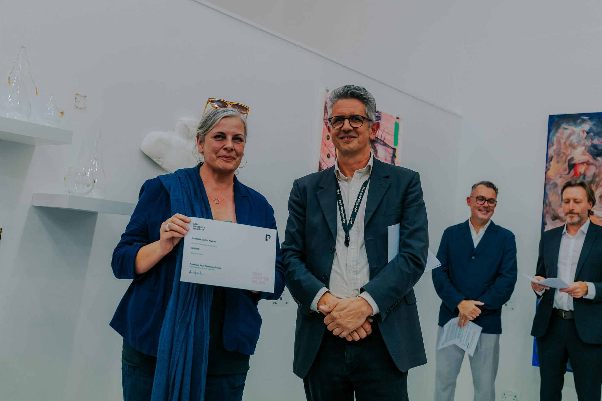 Marion Smylie left holds up her certificate with Prof Stephen Felmingham on the right of her while Dr Stephen Paige and Prof Paul Fieldsend Danks look on from the background