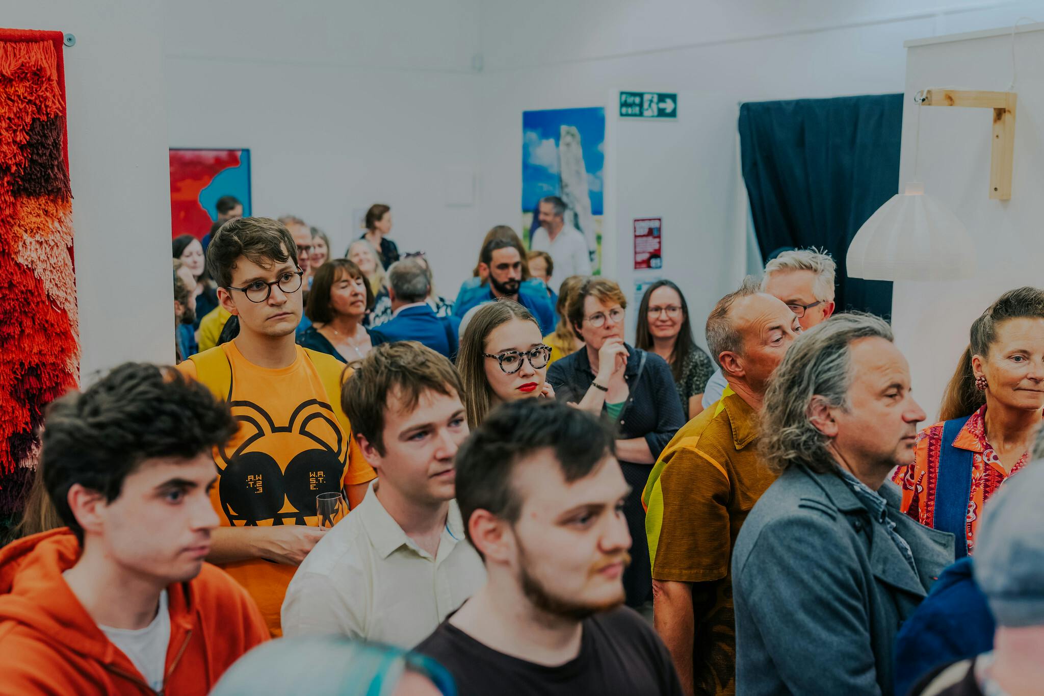 A crowd of people in the exhibition space with colourful paintings to the left and right