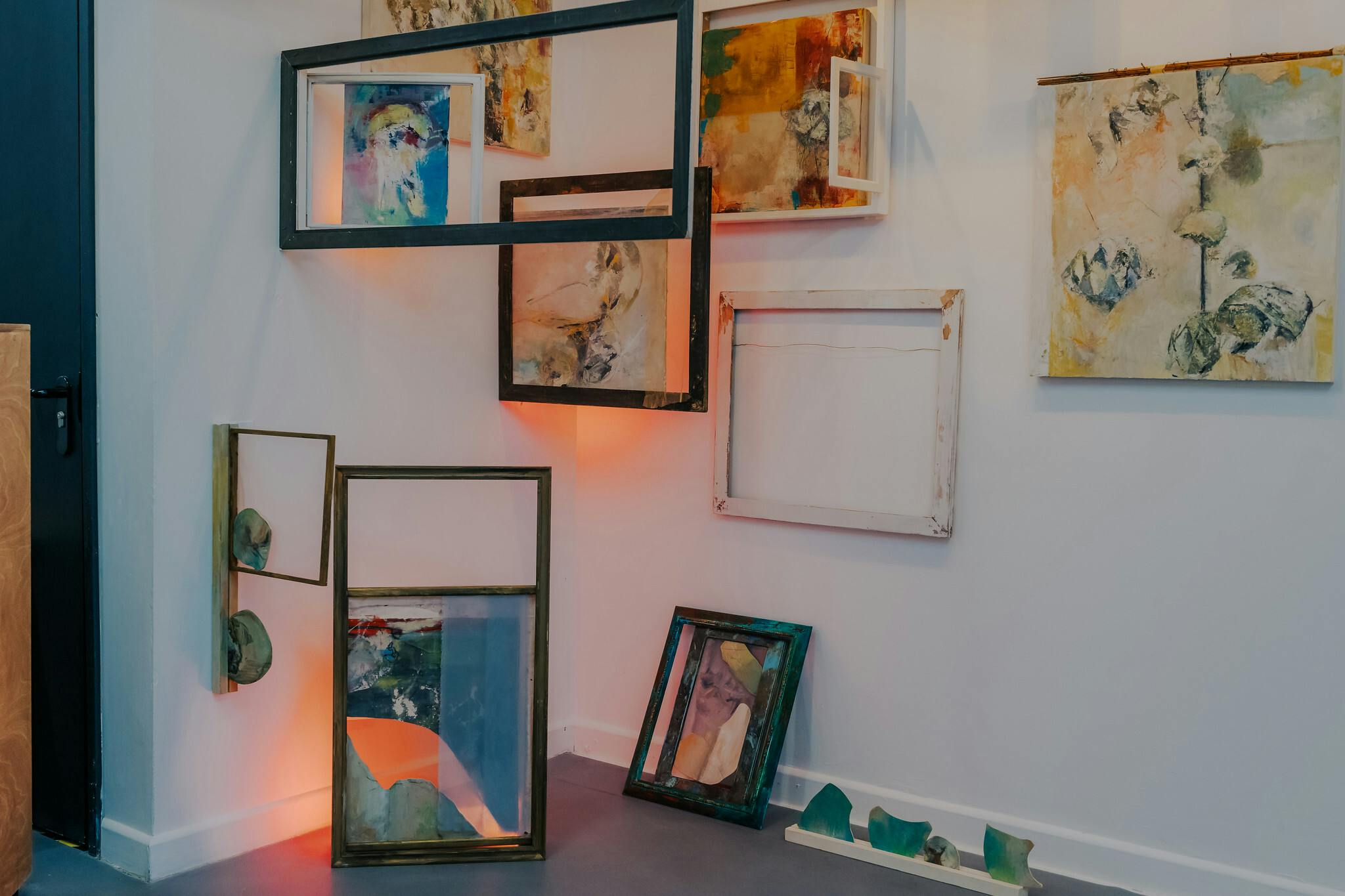 A number of paintings and frames backlit and positioned in a corner of a space with white walls and soft orange lighting