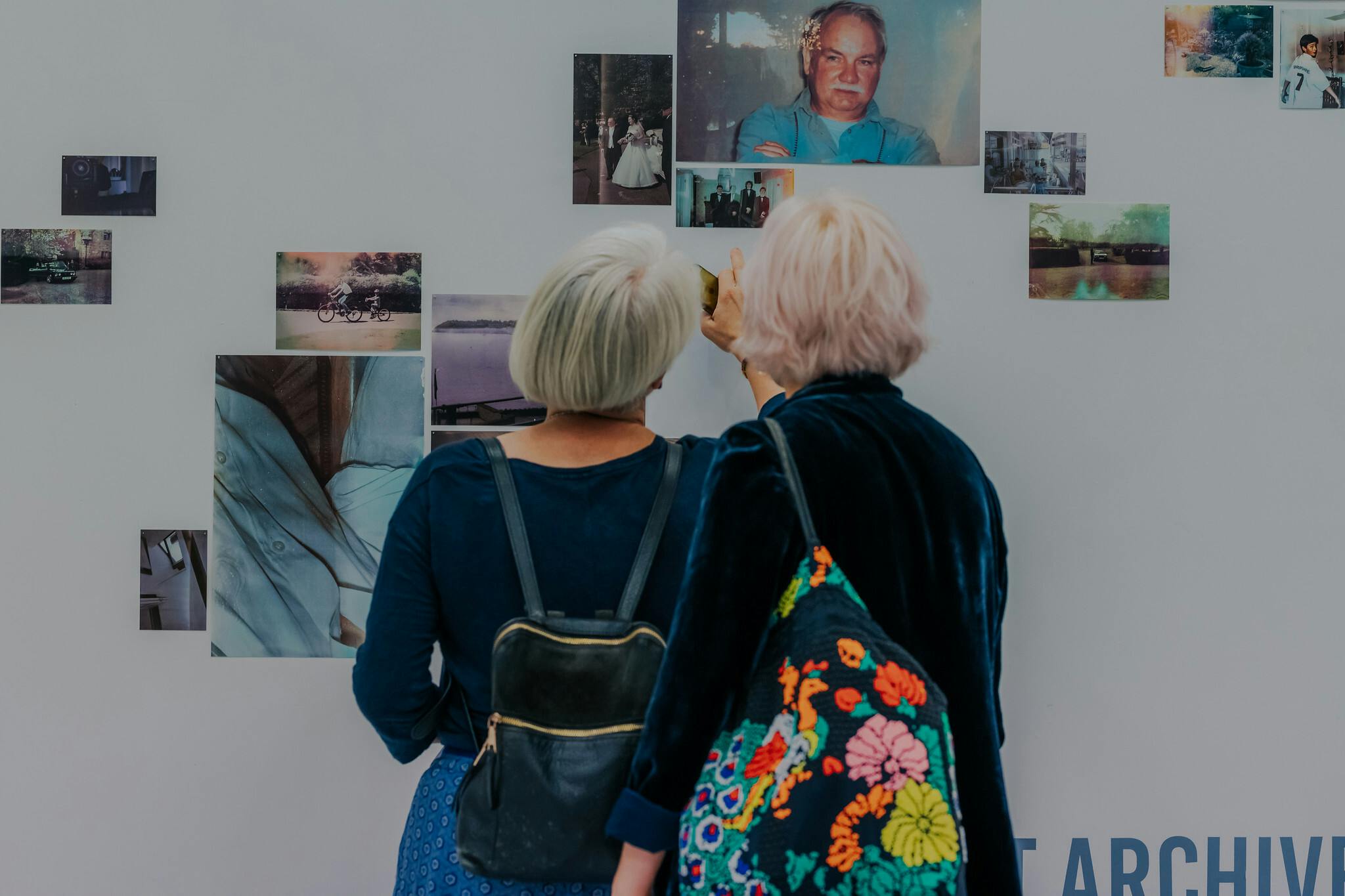 Two older women looking at and pointing at photos mounted on a white wall