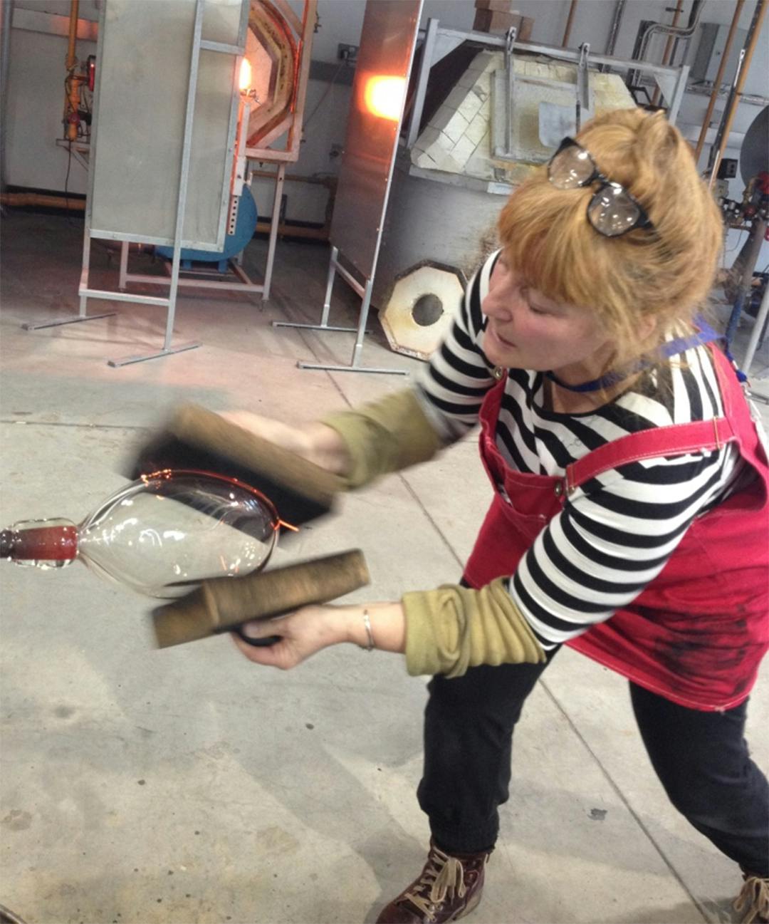 Jo Tyler uses two paddles to shape hot glass in our Glass Studios
